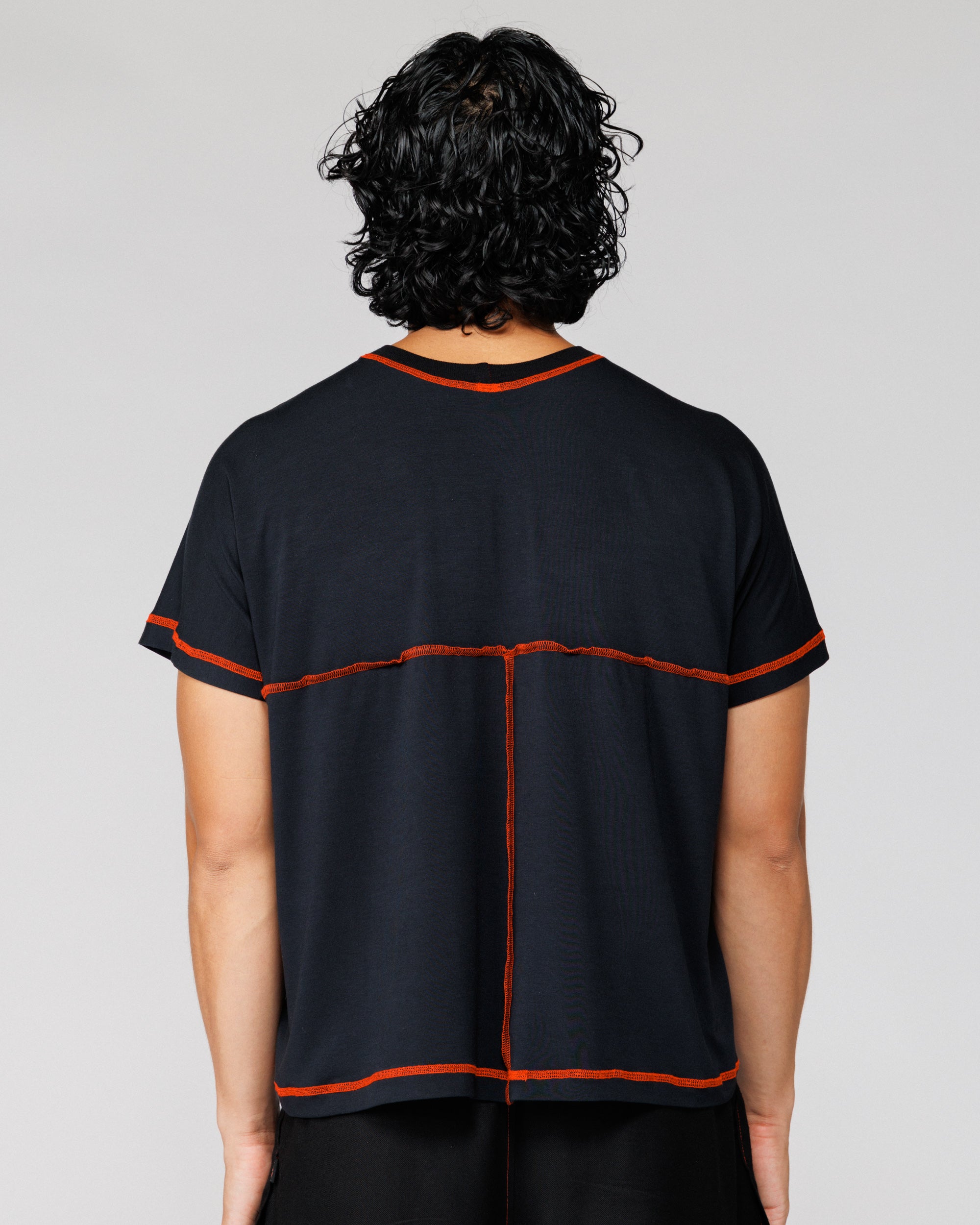 Model wearing Outnback Bog Tee in black, back view with orange cross-back seam detail