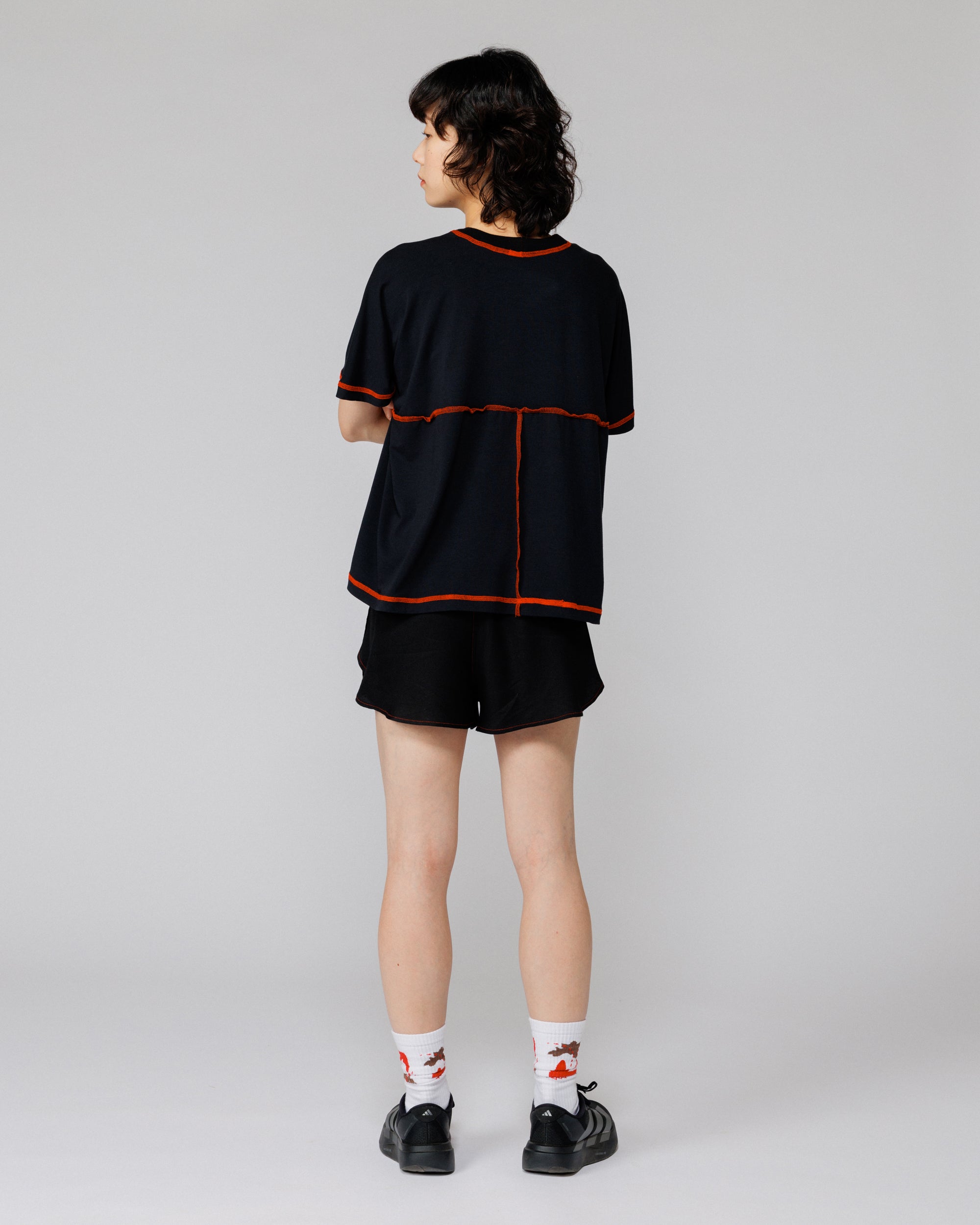 Model wearing Outnback Bog Tee in black, full-length back view showing orange contrast back seams