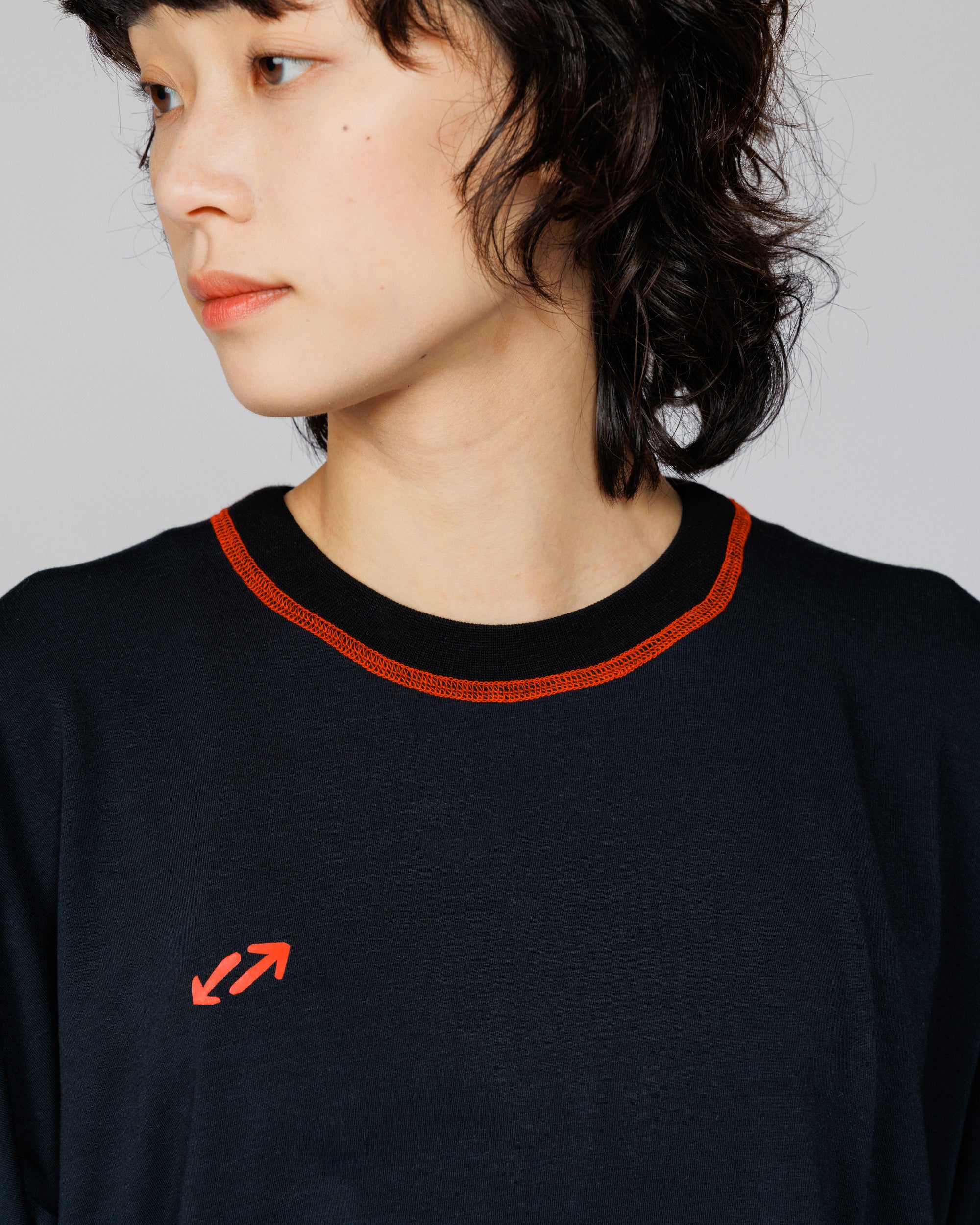 Close crop of Outnback Bog Tee in black on model, orange neckline stitching and red arrow logo