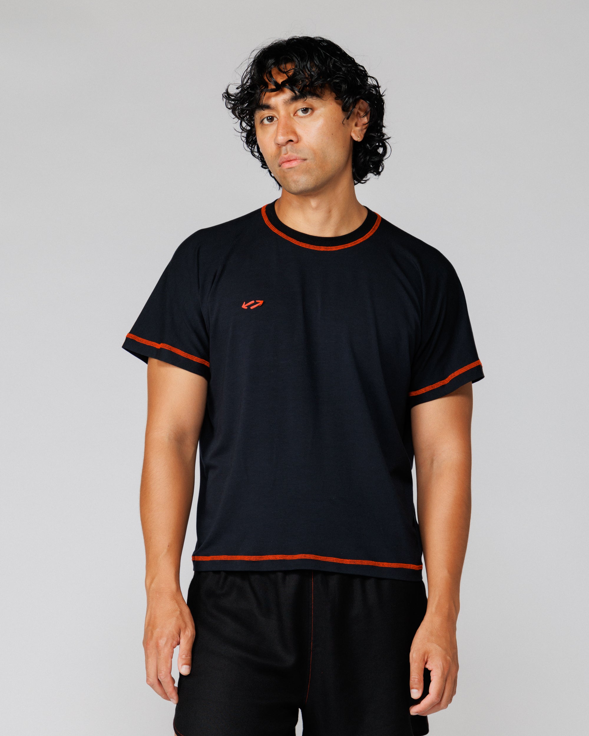 Model wearing Outnback Bog Tee in black, straight-on front view showing orange trim stitching