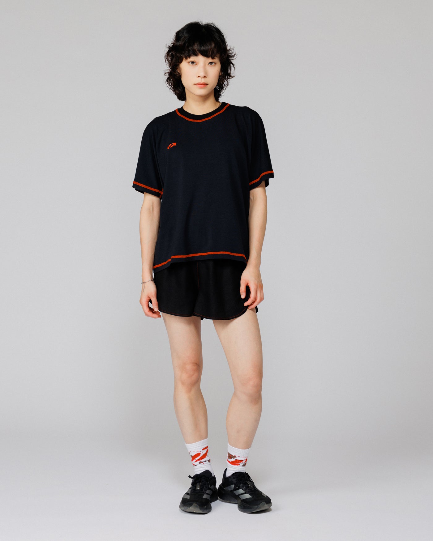 Model wearing Outnback Bog Tee in black, full-length front view with orange contrast overlock stitching