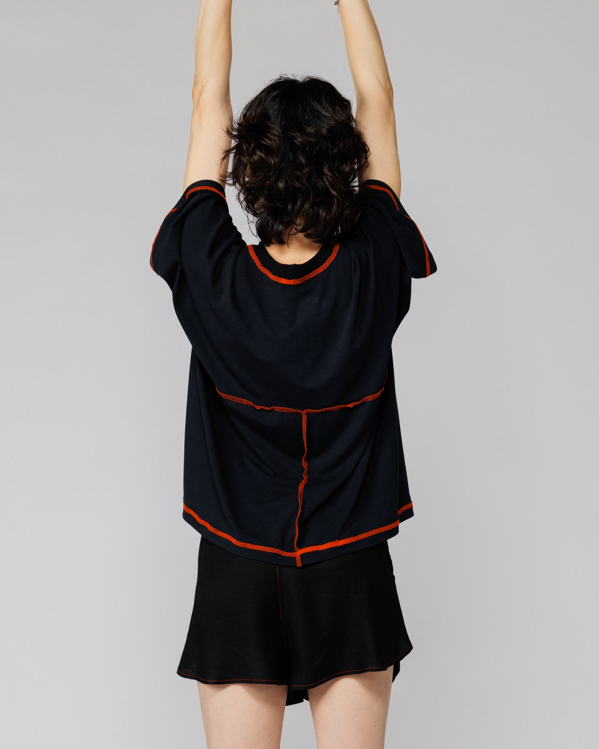 Model with arms raised in Outnback Bog Tee in black, back view showing range of movement