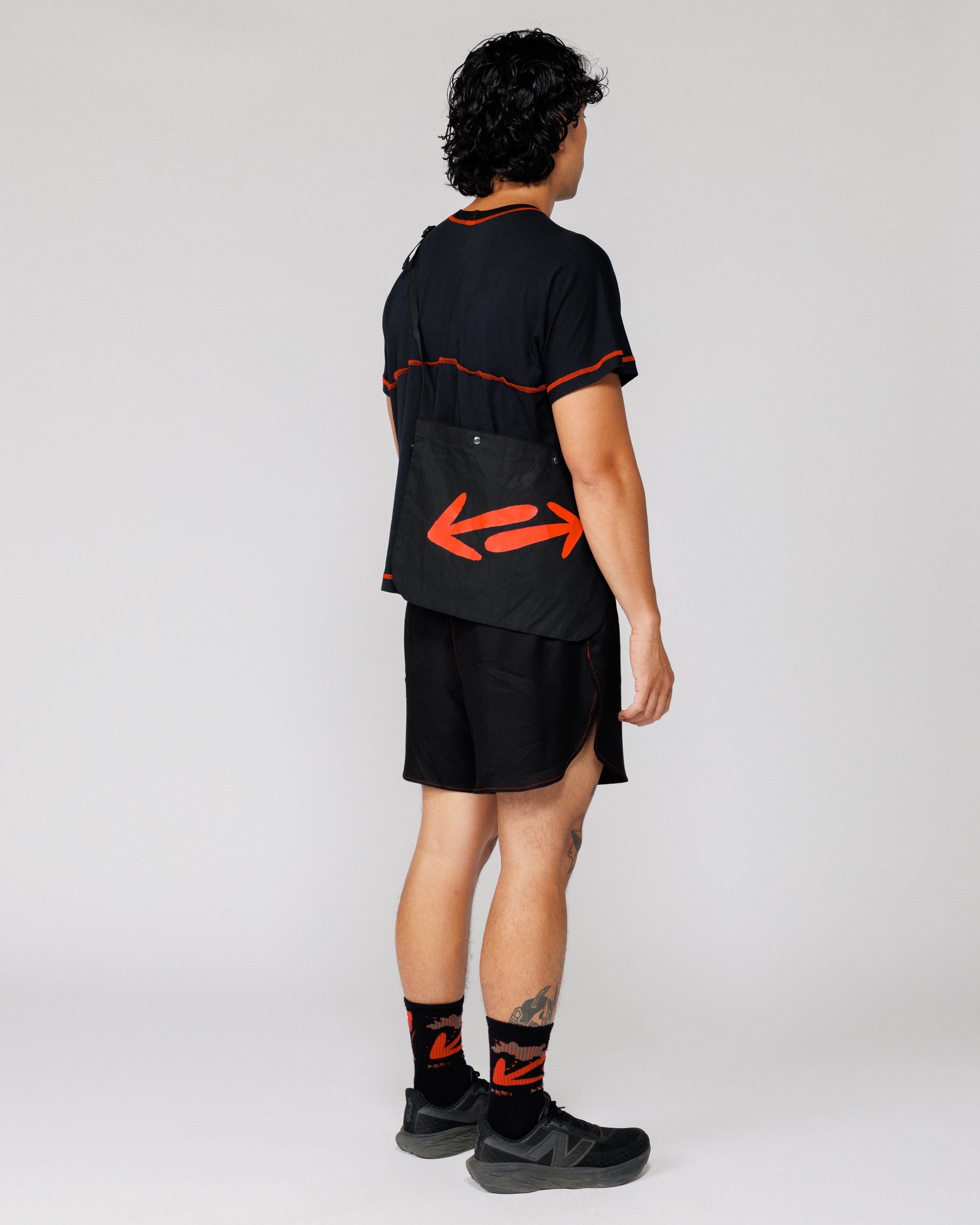 Model wearing the Outnback Musette in black, full-body back view showing red double-arrow print