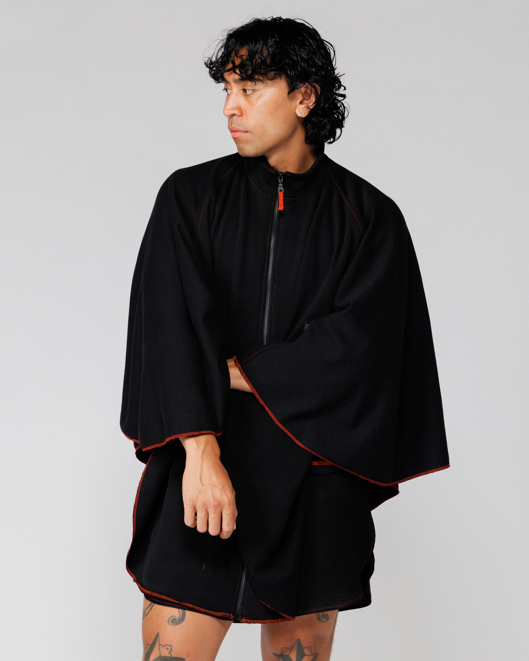 Outnback Recovery Cape in black worn by model, cropped front view with arm across body