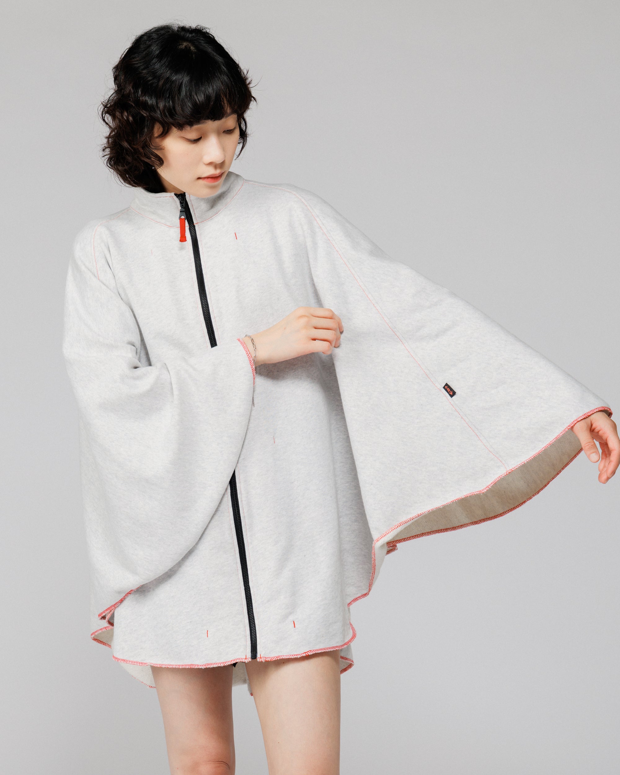 Cropped view of the Outnback Recovery Cape in marl grey held open to show the cream loopback interior and arrow logo tab