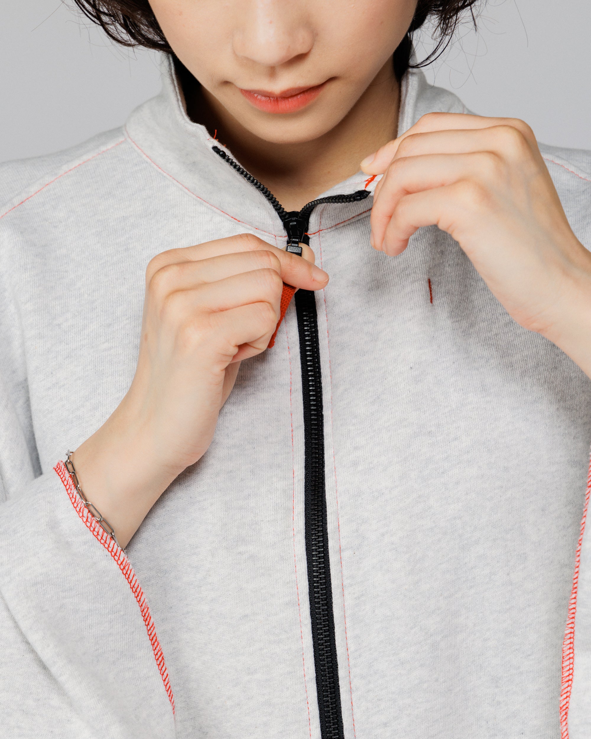 Close-up of the model pulling the front zip of the Outnback Recovery Cape in marl grey
