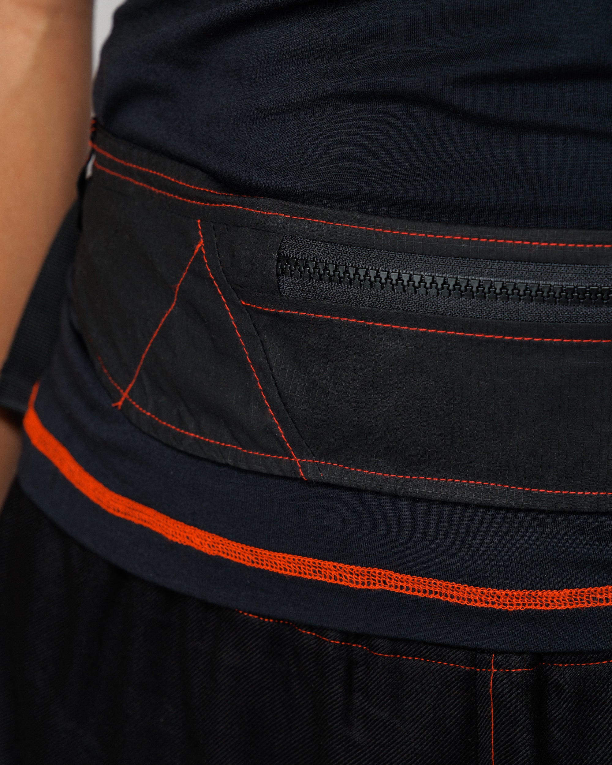 Close detail of the Outnback Running Strap in black zip pocket and red contrast stitching, worn