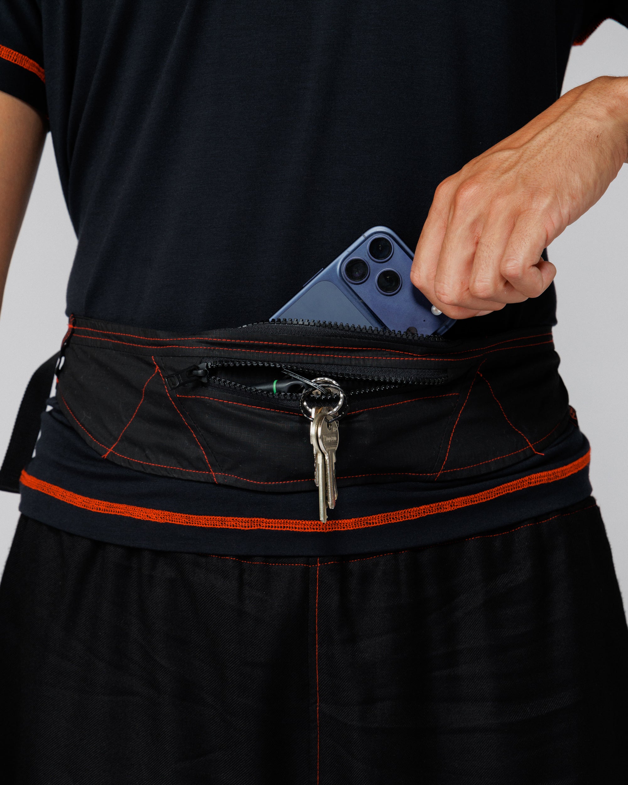 Cropped view of the Outnback Running Strap in black worn at the waist with a phone and keys stowed