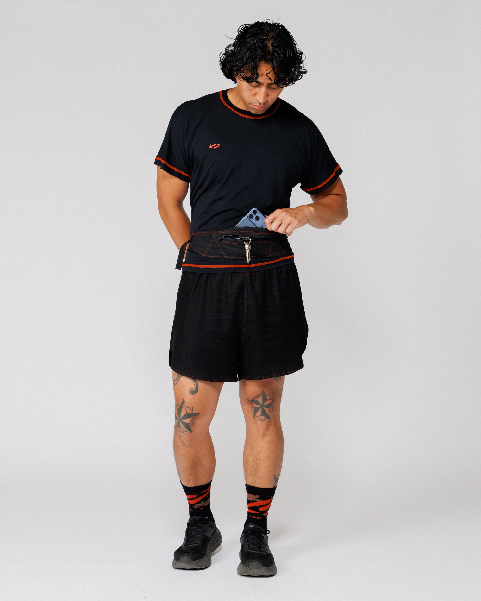 Model sliding a phone into the zip pocket of the Outnback Running Strap in black, full length